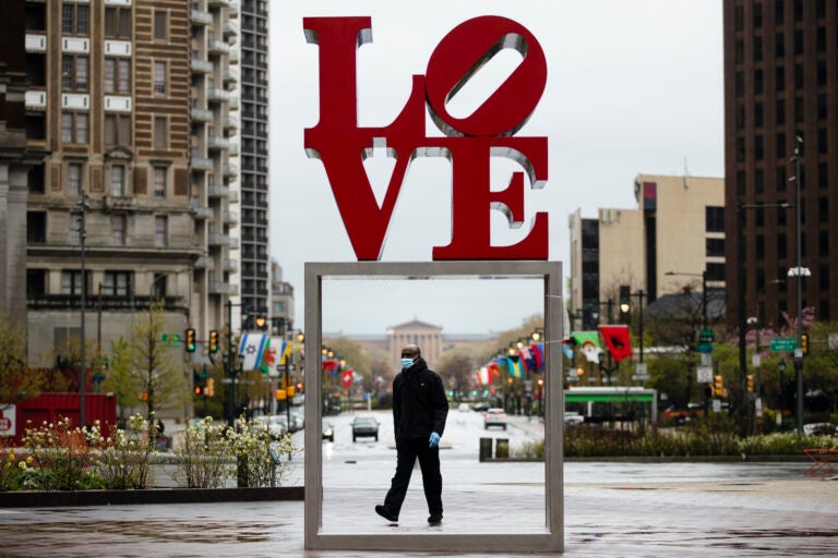 A person wearing a protective face mask and gloves as a precaution against the coronavirus walks through Love Park, in Philadelphia, Monday, April 13, 2020. (Matt Rourke/AP Photo)