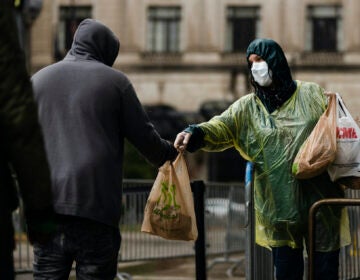 Kris Jaeger with Broad Street Ministry distributes food as part of a new initiative called Step Up to the Plate, during a rainstorm outside of City Hall in Philadelphia, Monday, April 13, 2020. (AP Photo/Matt Rourke)