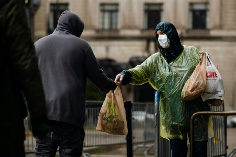 Kris Jaeger with Broad Street Ministry distributes food as part of a new initiative called Step Up to the Plate, during a rainstorm outside of City Hall in Philadelphia, Monday, April 13, 2020. (AP Photo/Matt Rourke)