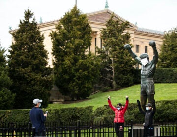 People wearing a protective face masks as a precaution against the coronavirus take photos with the Rocky statue outfitted with mock surgical face mask at the Philadelphia Art Museum in Philadelphia, Tuesday, April 14, 2020. (AP Photo/Matt Rourke)