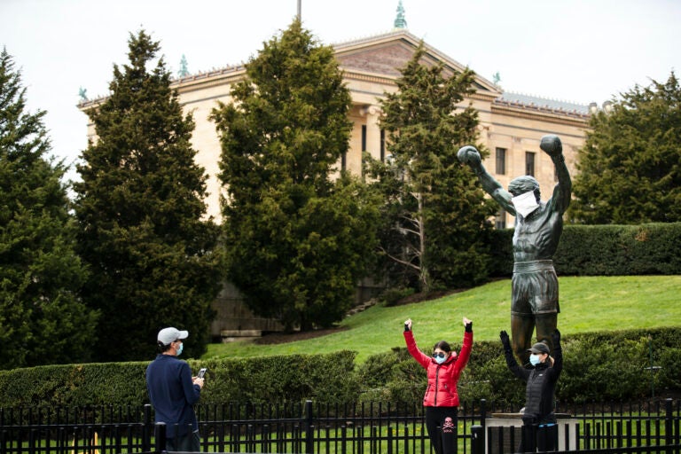 People wearing a protective face masks as a precaution against the coronavirus take photos with the Rocky statue outfitted with mock surgical face mask at the Philadelphia Art Museum in Philadelphia, Tuesday, April 14, 2020. (AP Photo/Matt Rourke)