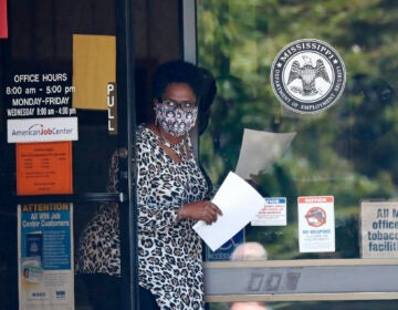 A masked worker at this state WIN job center in Pearl, Miss., holds an unemployment benefit application form as she waits for a client, Tuesday, April 21, 2020. (AP Photo/Rogelio V. Solis)