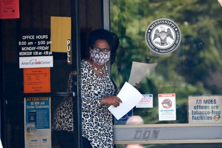 A masked worker at this state WIN job center in Pearl, Miss., holds an unemployment benefit application form as she waits for a client, Tuesday, April 21, 2020. (AP Photo/Rogelio V. Solis)