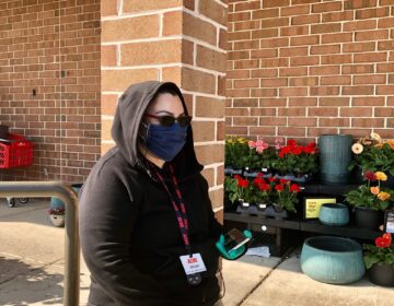 Miriam Casillas stands guard outside the Acme in Pike Creek, making sure shoppers are wearing a mask. (Cris Barrish/WHYY)