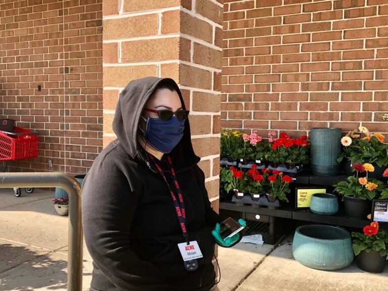 Miriam Casillas stands guard outside the Acme in Pike Creek, making sure shoppers are wearing a mask. (Cris Barrish/WHYY)