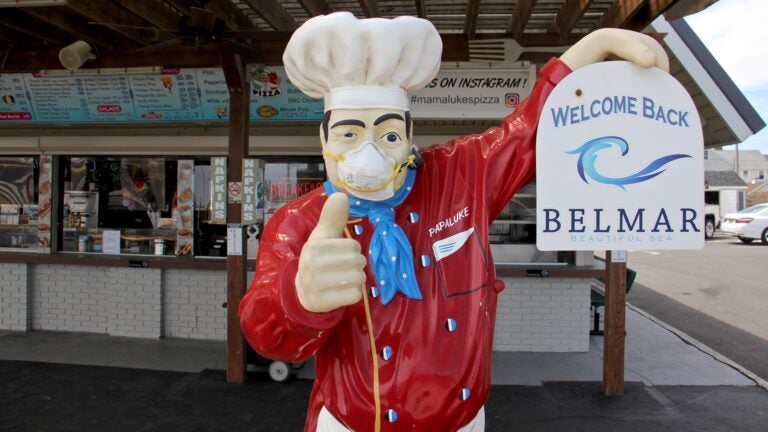 A figure in front of Mamalukes Pizza on Ocean Avenue in Belmar wears a protective mask. (Emma Lee/WHYY)