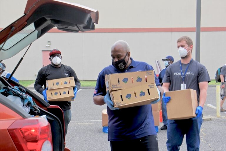 Camden County Freeholder Jon Young (center) and other volunteers and county employees carry boxes of fresh fruit and milk to a waiting car at Antioch Baptist Church.  (Emma Lee/WHYY)