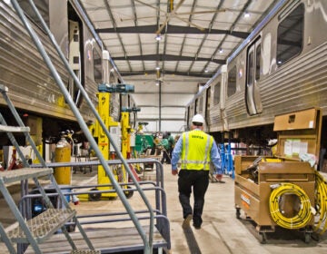 A SEPTA employee  walks between two El cars lifted for repairs at the 69th Street SEPTA repair shop. (Kimberly Paynter/WHYY)