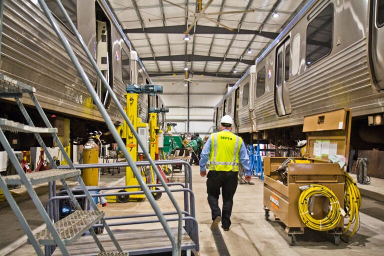 A SEPTA employee  walks between two El cars lifted for repairs at the 69th Street SEPTA repair shop. (Kimberly Paynter/WHYY)