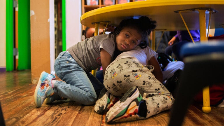 Justice Buress, 4, hides under a table while demonstrating a drill at Little Explorers Learning Center in St. Louis. Tess Trice, head of the day care program, carries out monthly drills to train the children to get on the floor when they hear gunfire.