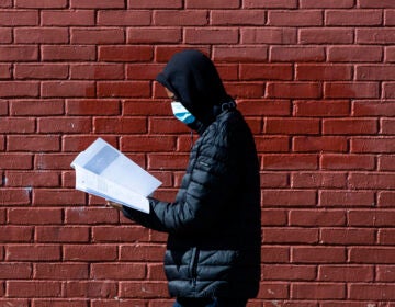 In this Thursday, March 26, 2020, photo, Terrell Bell, wearing a protective face mask, looks at a learning guide he picked up for his little sister at John H. Webster Elementary School in Philadelphia. (AP Photo/Matt Rourke)