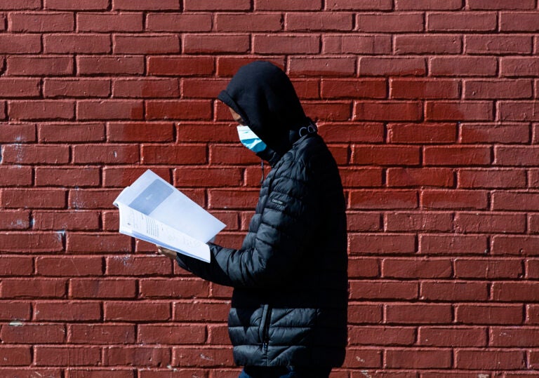 In this Thursday, March 26, 2020, photo, Terrell Bell, wearing a protective face mask, looks at a learning guide he picked up for his little sister at John H. Webster Elementary School in Philadelphia. (AP Photo/Matt Rourke)