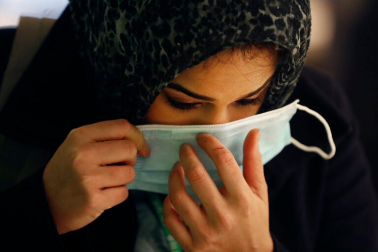 In this Wednesday, April 22, 2020, RUSH Hospital respiratory therapist Jumana Azam puts on a surgical mask after standing before a face temperature scanner as she reports for her early morning shift at the hospital in Chicago. (AP Photo/Charles Rex Arbogast)