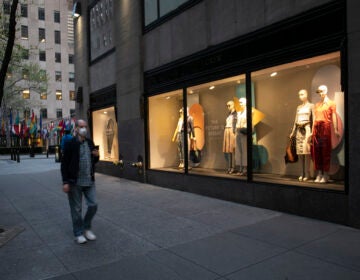 A man wearing a mask walks by a window display at a J Crew store in Rockefeller Center, Saturday, May 2, 2020, in New York. On April 30, the company announced it would apply for bankruptcy protection amidst the COVID-19 pandemic.  (AP Photo/Mark Lennihan)