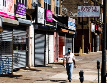 A person wearing a protective face mask as a precaution against the coronavirus walks past stuttered businesses in Philadelphia, Thursday, May 7, 2020. (AP Photo/Matt Rourke)