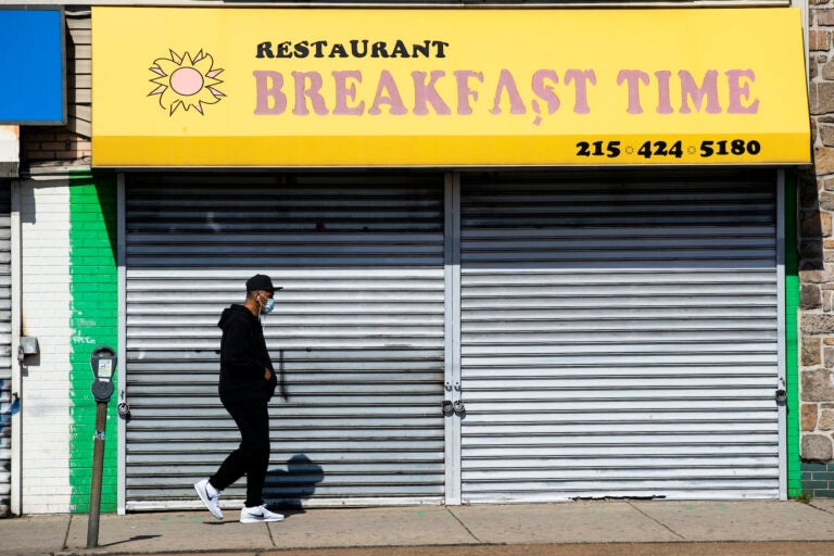 A person wearing a protective face mask as a precaution against the coronavirus walks past a shuttered business in Philadelphia, Thursday, May 7, 2020. (AP Photo/Matt Rourke)