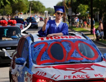 Thomas Harden rings a cowbell as he stands up through the vehicles sun roof waving a supporters during a neighborhood parade honoring 2020 student graduates from both J.J. Pearce and Richardson High Schools in Richardson, Texas, Saturday, May 9, 2020.  (AP Photo/Tony Gutierrez)