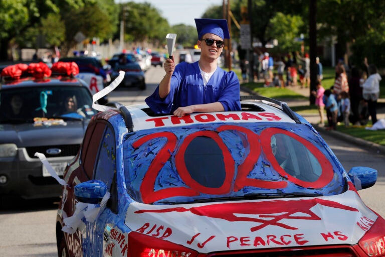 Thomas Harden rings a cowbell as he stands up through the vehicles sun roof waving a supporters during a neighborhood parade honoring 2020 student graduates from both J.J. Pearce and Richardson High Schools in Richardson, Texas, Saturday, May 9, 2020.  (AP Photo/Tony Gutierrez)