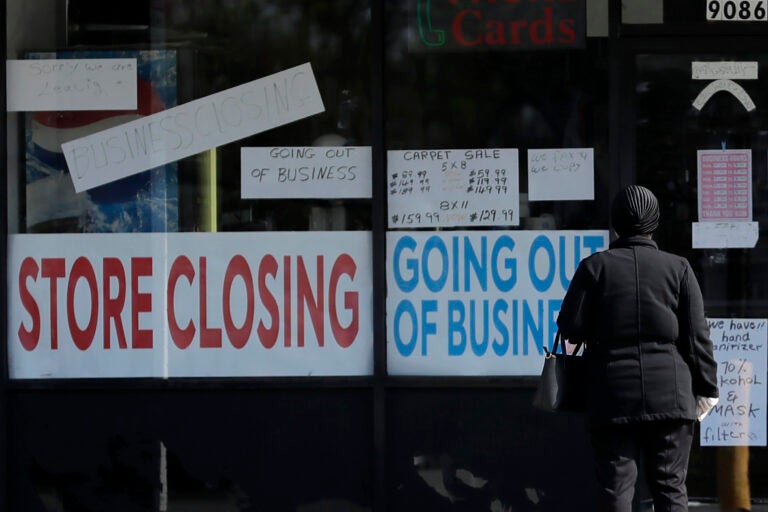 A woman looks at signs at a store closed due to COVID-19. (AP Photo/Nam Y. Huh)