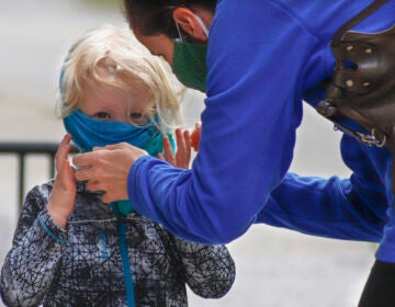 Bridget Kreider, right, helps her three-year-old daughter Maggie pull on her protective face covering before entering a store, Wednesday, May 20, 2020, in Harmony, Pa. Customers entering stores are required to wear face coverings to help prevent the spread of the new coronavirus during the COVID-19 pandemic under the state yellow phase reopening guide. (AP Photo/Keith Srakocic)