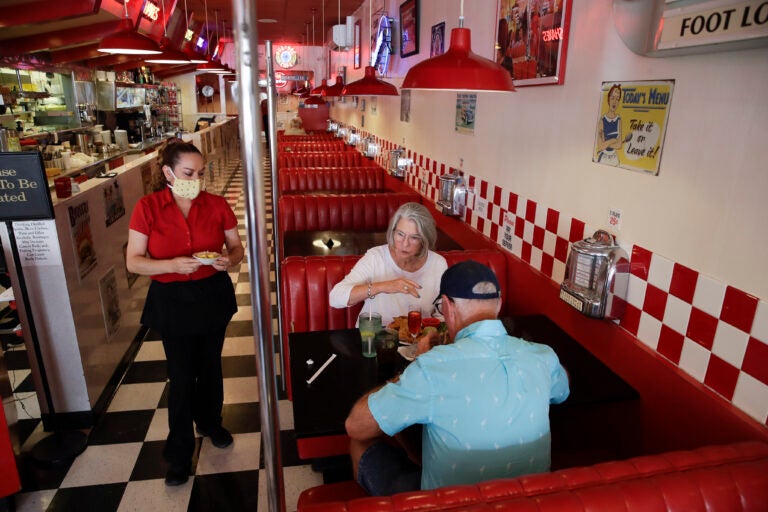 Lynn Tanner, center, and her husband Ryan, bottom right, are served lunch at Busy Bee Cafe Thursday, May 21, 2020, in Ventura, Calif.  Much of the country remains unlikely to venture out to bars, restaurants, theaters or gyms anytime soon, despite state and local officials increasingly allowing businesses to reopen. That's according to a new survey by The Associated Press-NORC Center for Public Affairs Research. (AP Photo/Marcio Jose Sanchez)