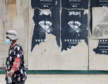 A woman walks past a boarded up business, Thursday, May 28, 2020, in East Cleveland, Ohio. (AP Photo/Tony Dejak)