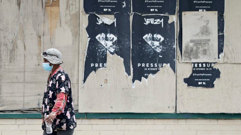 A woman walks past a boarded up business, Thursday, May 28, 2020, in East Cleveland, Ohio. (AP Photo/Tony Dejak)