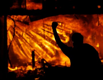 A protester gestures in front of the burning 3rd Precinct building of the Minneapolis Police Department on Thursday, May 28, 2020, in Minneapolis. (AP Photo/Julio Cortez)