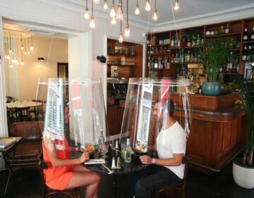 A man and a woman demonstrate dining under a plastic shield amid coronavirus pandemic