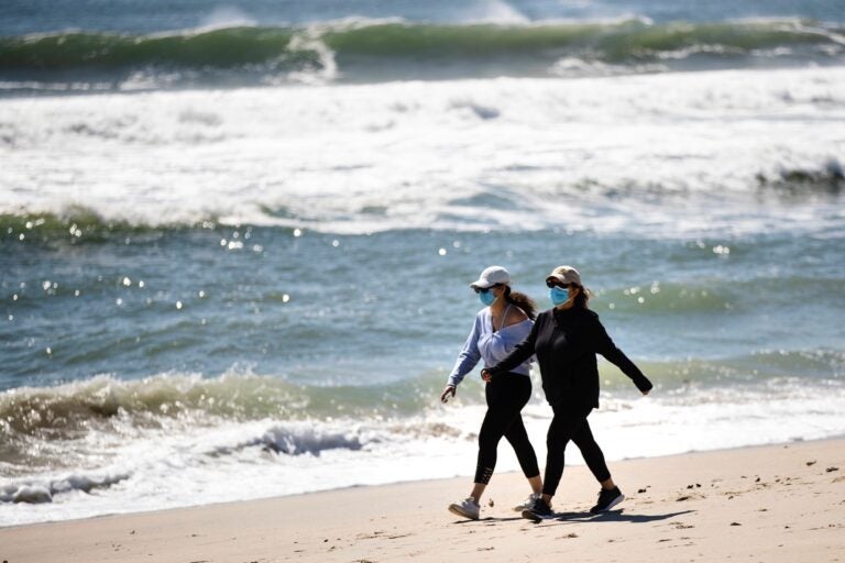 People wearing a protective face masks as a precaution against the coronavirus walk on the beach in Belmar, N.J., Saturday, May 2, 2020. (AP Photo/Matt Rourke)