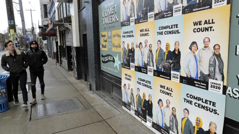 People walk past posters encouraging participation in the 2020 census in April in Seattle. A group of House Democrats have introduced a bill that would grant the U.S. Census Bureau's request to delay major deadlines for delivering results of the count because of the pandemic. (Ted S. Warren/AP Photo)