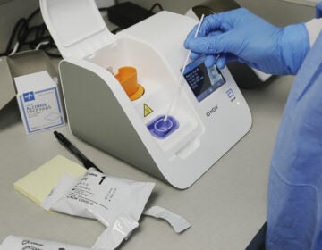 A lab technician dips a sample into the Abbott Laboratories ID Now testing machine at the Detroit Health Center on April 10, 2020. (Carlos Osorio/AP Photo)