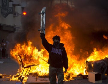 A protester holds a skateboard in front of a fire in Los Angeles, Saturday, May 30, 2020, during a protest over the death of George Floyd.