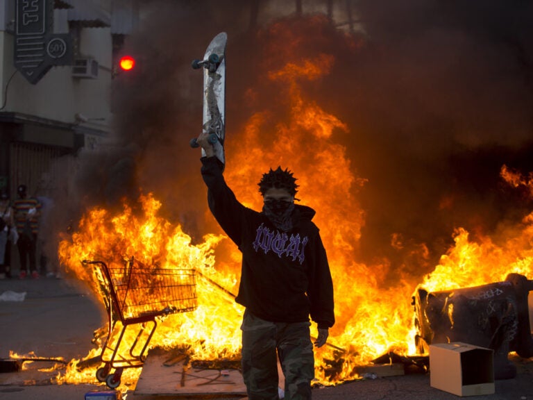 A protester holds a skateboard in front of a fire in Los Angeles, Saturday, May 30, 2020, during a protest over the death of George Floyd.