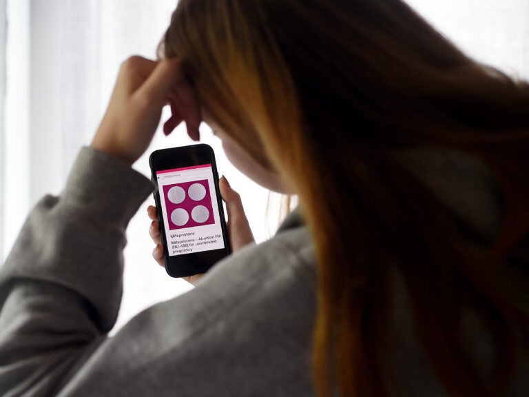 In this photo illustration, a person looks at an abortion pill (RU-486) for unintended pregnancy from Mifepristone displayed on a smartphone on May 8, 2020, in Arlington, Va. Under federal law, even in states where telemedicine abortion is legal, there are strict rules surrounding how the pill is dispensed. (Olivier Douliery/AFP via Getty Images)