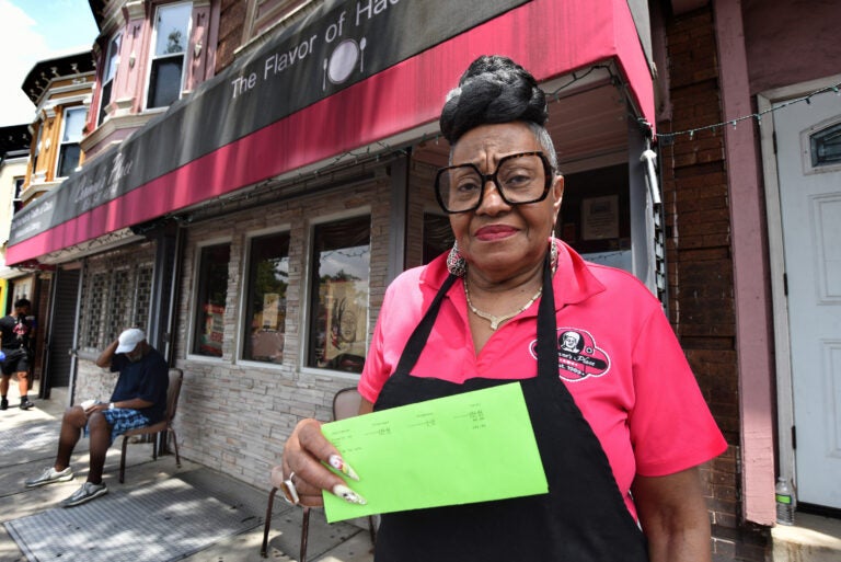 On June 5, Corinne Bradley-Powers, owner of Corinne's Place, stands in front of her popular Camden restaurant holding the notice she received that her restaurant would be on a list for sheriff's sale this month if she didn't pay the $282 she owed.  (Photo by April Saul for WHYY)