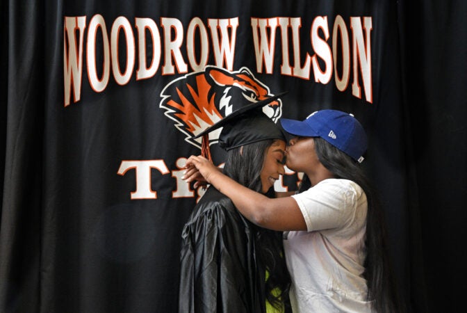 At Woodrow Wilson HS on June 24, graduate Domera Nunn gets a kiss from sister Quadire Wilson during a photo shoot. Nunn, who is headed for Rutgers in New Brunswick in the fall, said, 