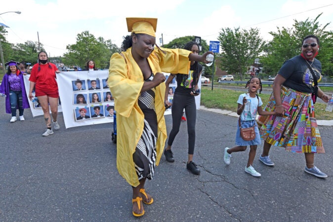 During the parade on June 26, Camden High graduate Zanabria Harris, 18, dances on Baird Boulevard; at right is parade organizer Ronsha Dickerson. (Photo by April Saul for WHYY)