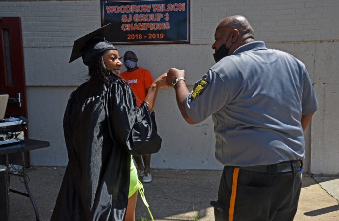 At Woodrow Wilson HS on June 24, graduate Damera Nunn fist-bumps a security officer on her way to pose for graduation photos.  (Photo by April Saul for WHYY)