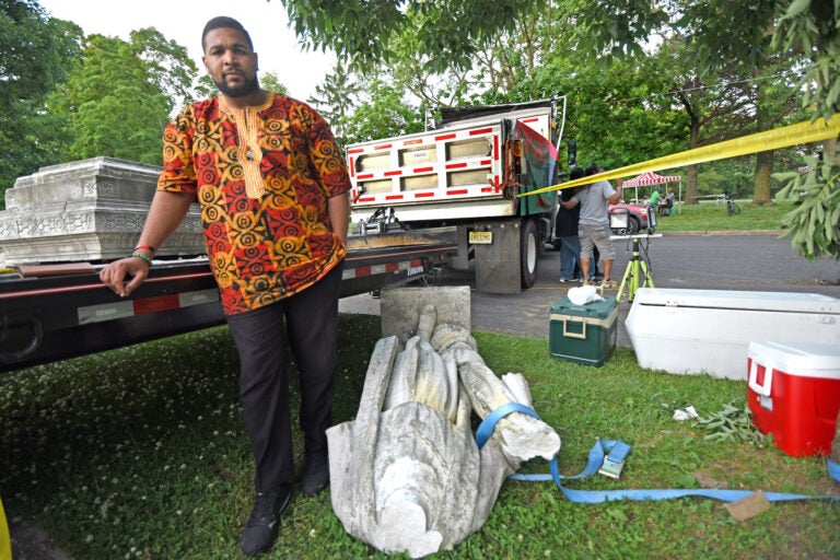 Pastor Levi Combs III of Camden's First Refuge Baptist Church, watches over pieces of the Christopher Columbus statue in Farnham Park on Friday, June 12, 2020. (April Saul for WHYY)