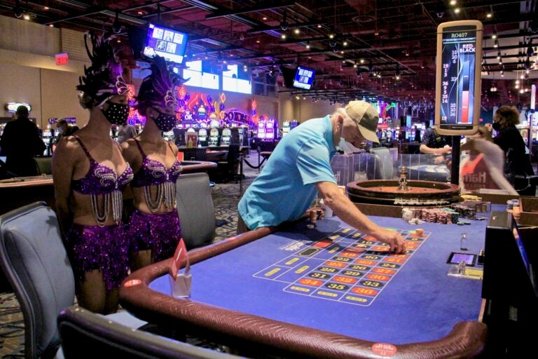Bob Mills of Wenonah, N.J., places a bet at Harrah's Philadelphia, attended by showgirls Vanessa Harkins and Angel Simpkins. (Emma Lee/WHYY)