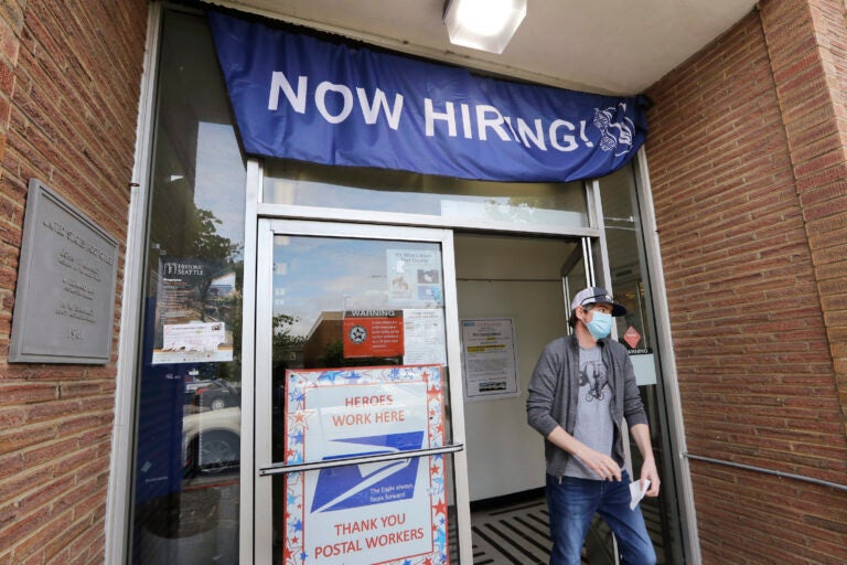 A customer walks out of a U.S. Post Office branch and under a banner advertising a job opening