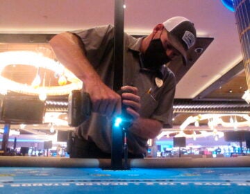 In this June 24, 2020 photo, Dean Loveland, a worker at the Hard Rock casino in Atlantic City N.J., installs plexiglass barriers between player positions at a card table at the casino a week before it was to reopen amid the coronavirus outbreak. Smoking, drinking and eating will all be prohibited when Atlantic City's casinos reopen after being shut for three months due to the coronavirus outbreak under rules imposed by New Jersey Gov. Phil Murphy on June 29, 2020. (AP Photo/Wayne Parry)