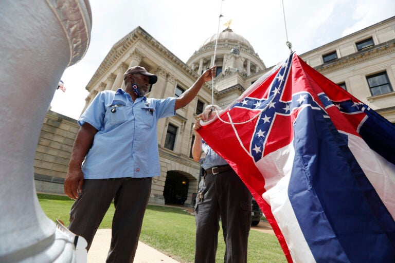 Mississippi Department of Finance and Administration employees Willie Townsend, left, and Joe Brown, attach a Mississippi state flag to the harness before raising it over the Capitol grounds in Jackson, Miss., Tuesday, June 30, 2020. (AP Photo/Rogelio V. Solis)