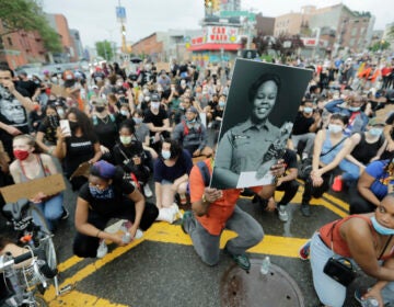 A man holds a photograph of Breonna Taylor on her birthday as he kneels with other protesters