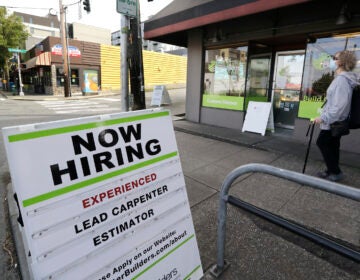 A pedestrian wearing a mask walks past reader board advertising a job opening for a remodeling company