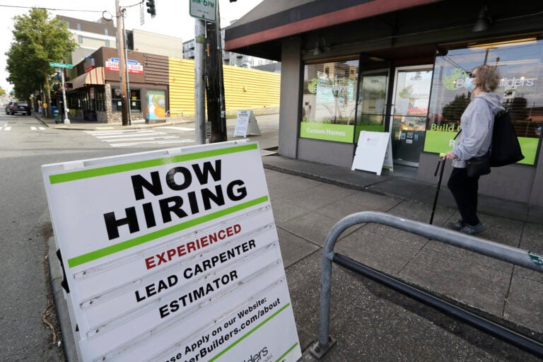 A pedestrian wearing a mask walks past reader board advertising a job opening for a remodeling company
