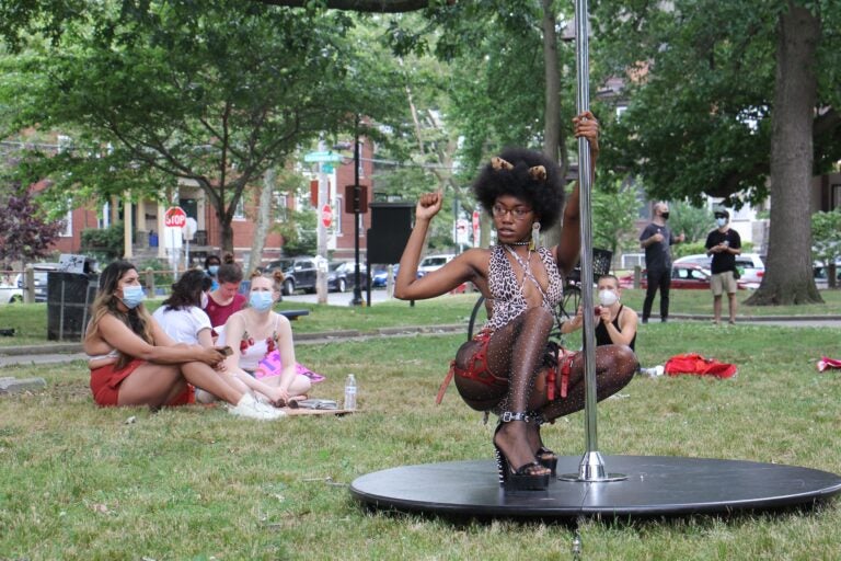 A dancer known by the professional name Tabz poses with a dance pole at Malcolm X Park. She is a leader of the group Stiletto, which held an event in the park to advocate for better working conditions for dancers and sex workers. (Emma Lee/WHYY)