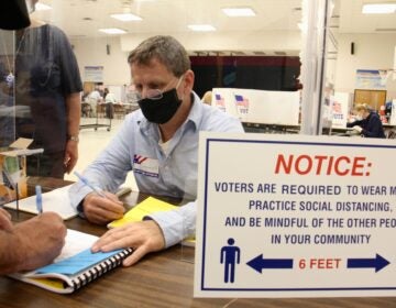 Poll worker Chuck Kellander interacts with voters through a plexiglass screen at Belmont Hill Elementary School in Bensalem, Bucks County. (Emma Lee/WHYY)