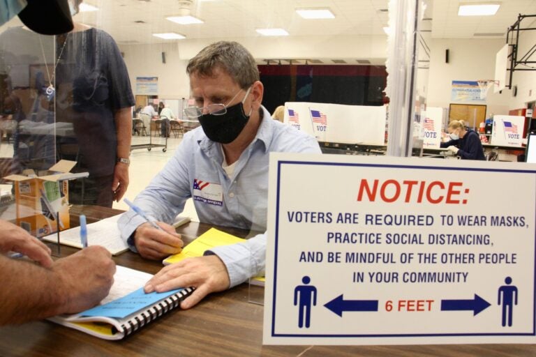 Poll worker Chuck Kellander interacts with voters through a plexiglass screen at Belmont Hill Elementary School in Bensalem, Bucks County. (Emma Lee/WHYY)